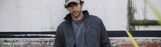 A man is standing outside, wearing a grey Ayacucho jacket and a grey Ayacucho cap. 