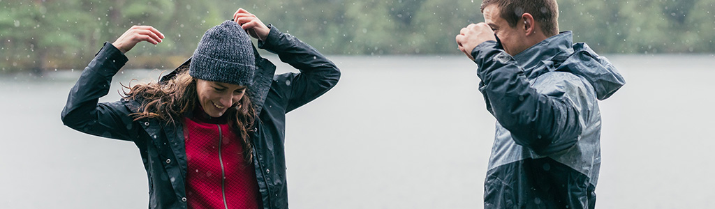 Two people are standing by a lake in a rain / snow, wearing Columbia clothing.