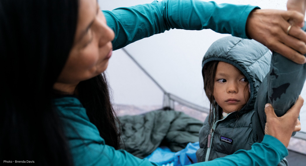A woman sews a patch into the arm of a Patagonia jacket on a young child