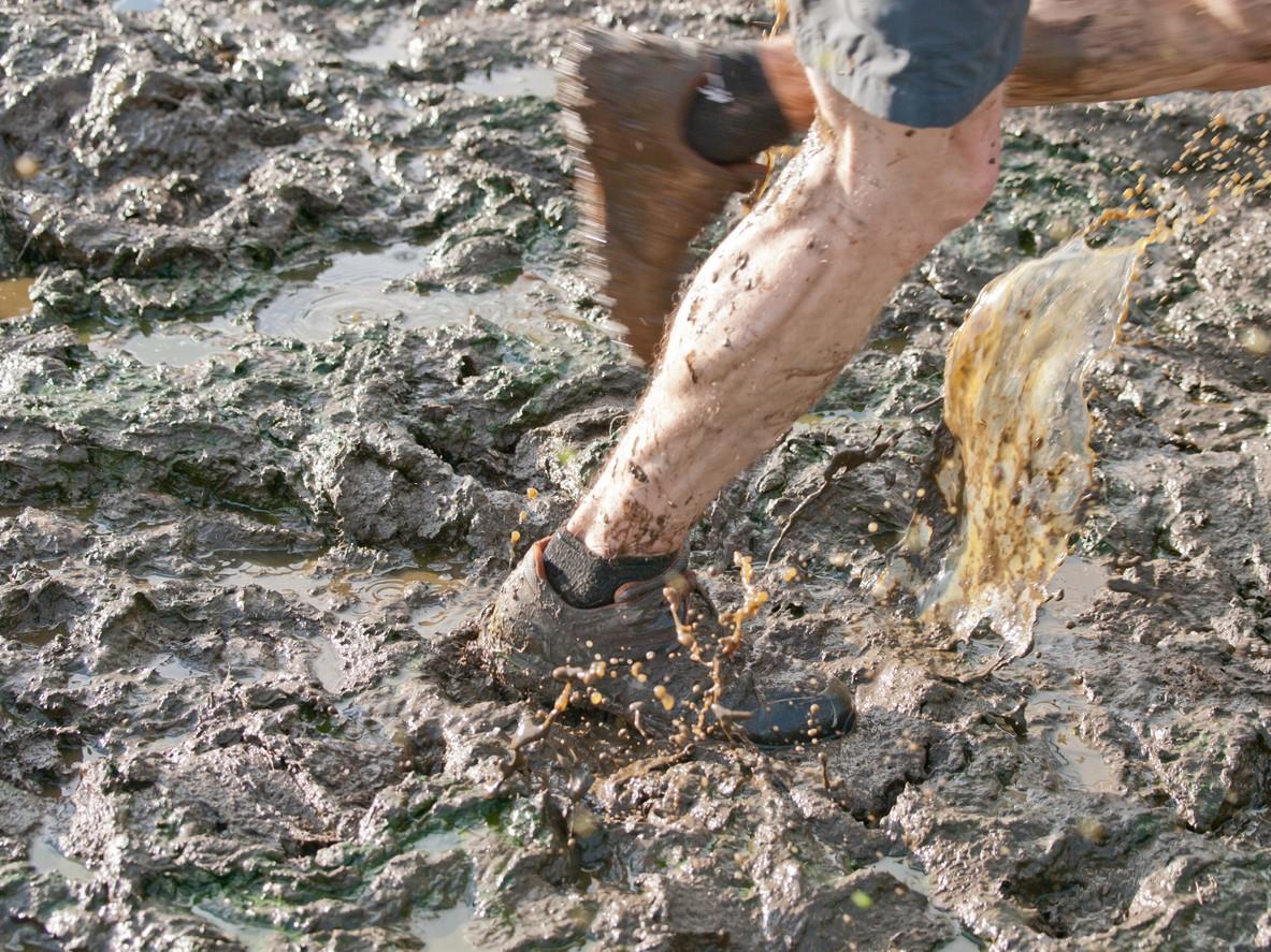 A person's running shoes covered in mud on a trail run 