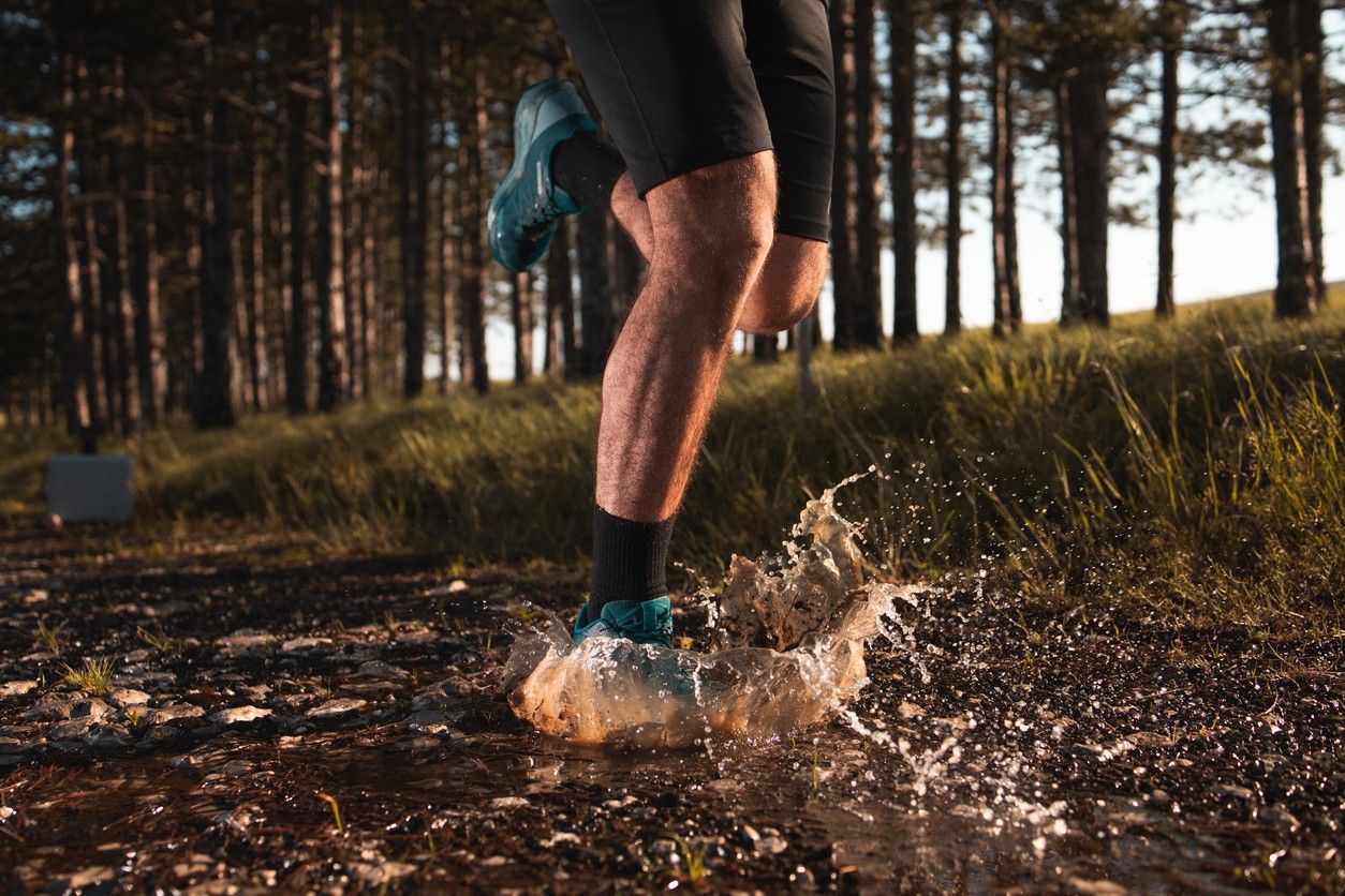 A person splashing in a puddle on a trail run 