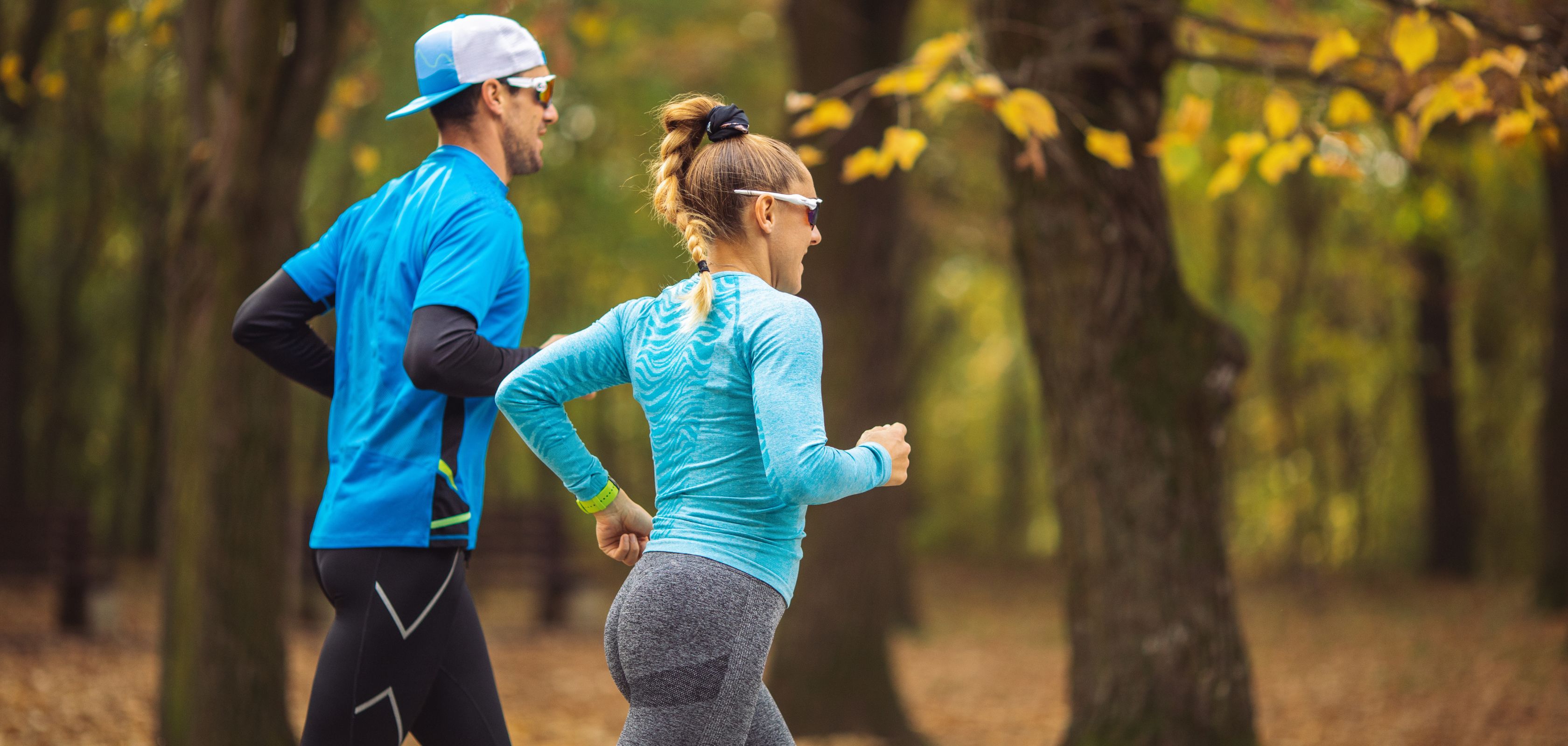 Two people wearing blue running through the forest in autumn with yellow-leaved trees