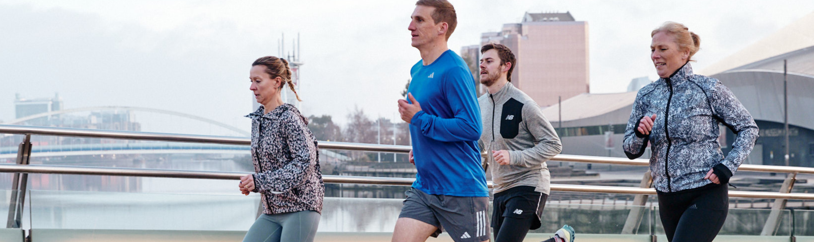 A group of people in running clothes running across a bride in the city