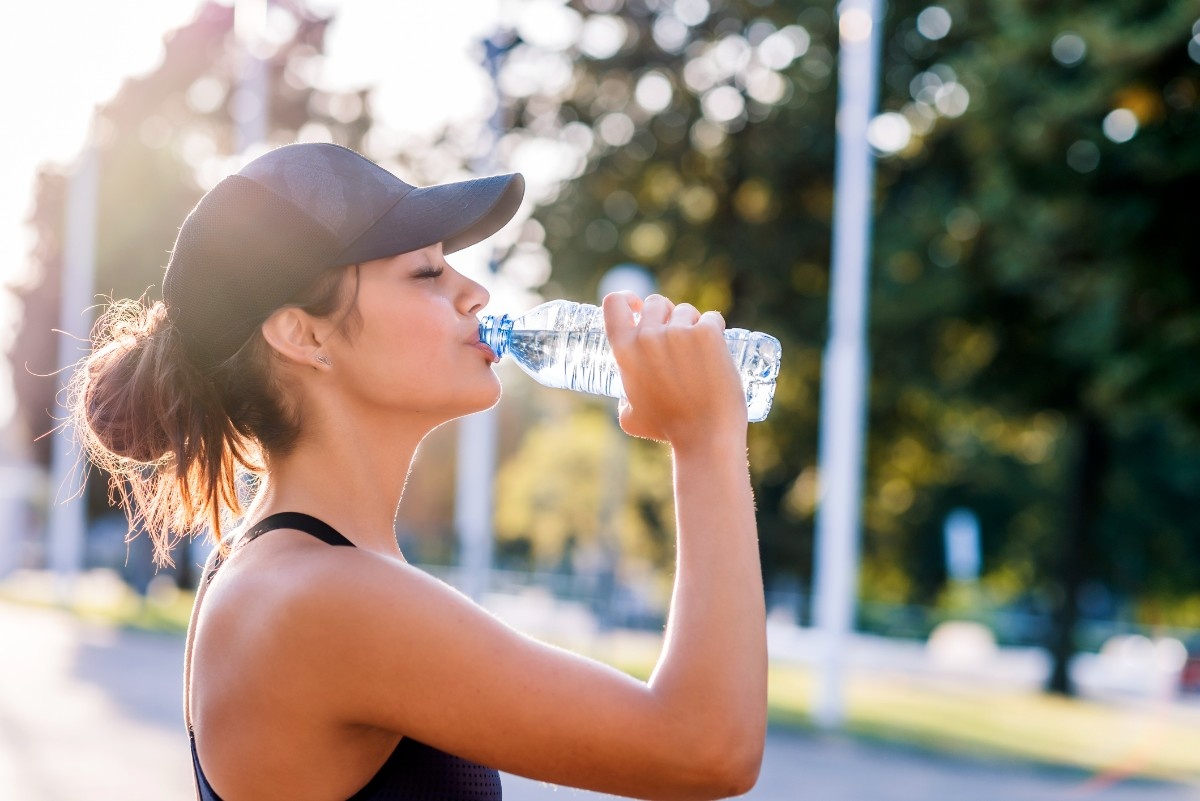 A woman on a run drinking from a water bottle in a running cap 