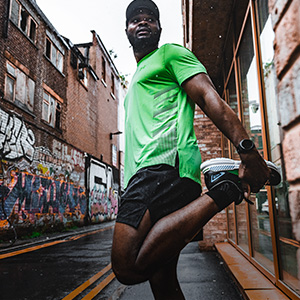 Shop clothing. A man in green Tshirt and black shorts stretching before the run