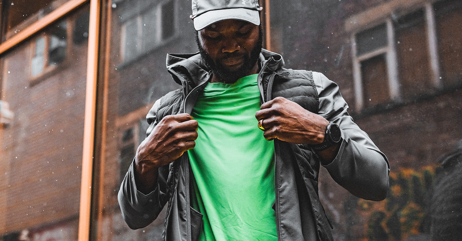 Shop men's running gear. A man adjusting his jacket over green t-shirt